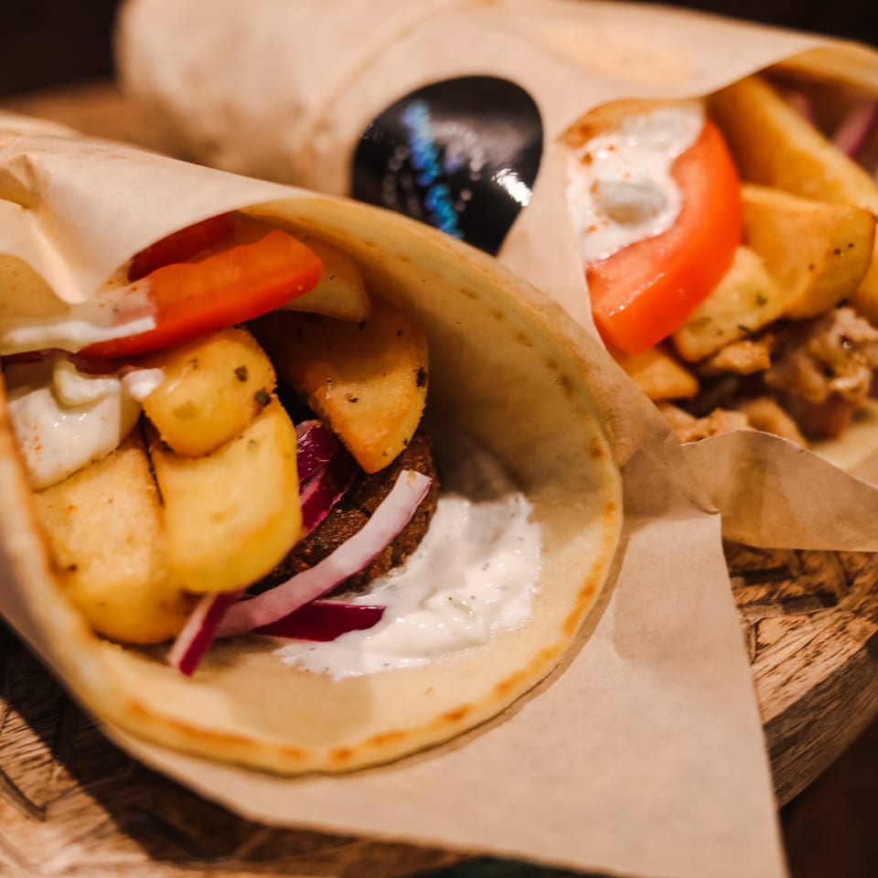 Two Spyro's Gyros, one with falafel, fries, red onion, tomato, and tzatziki sauce.