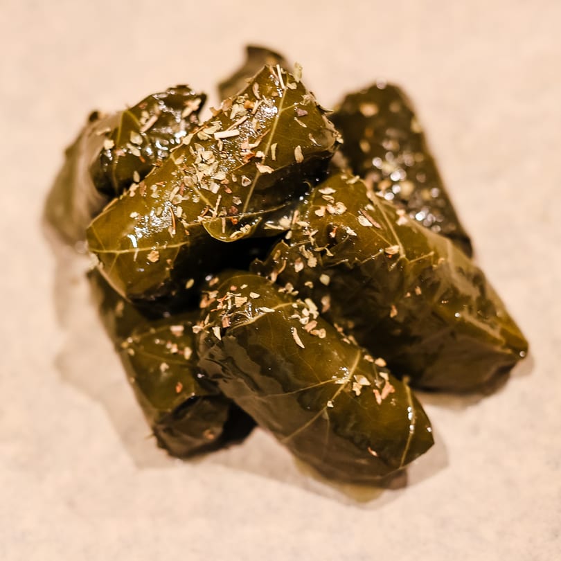 Close-up of several Greek dolmades, grape leaves stuffed with rice and herbs, sprinkled with seasoning.