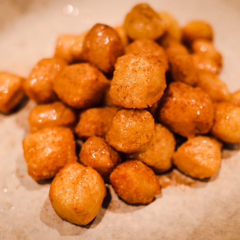 A close-up of golden-brown Loukoumades, Greek honey puffs, dusted with cinnamon on a light plate.
