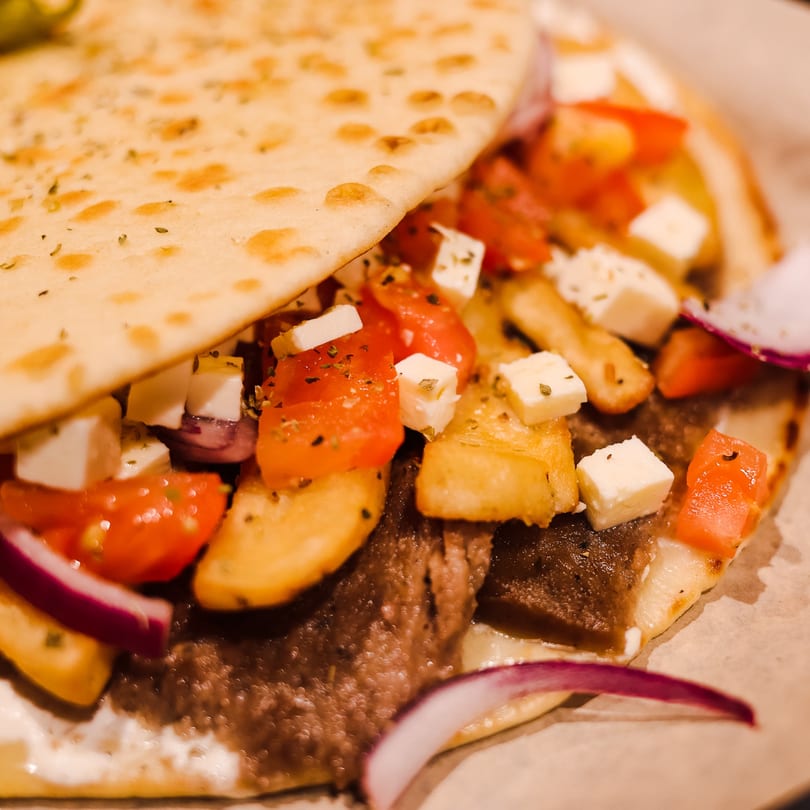 Close-up of a Spyro's Gyro with meat, tomatoes, feta, fries, and red onion on pita bread.