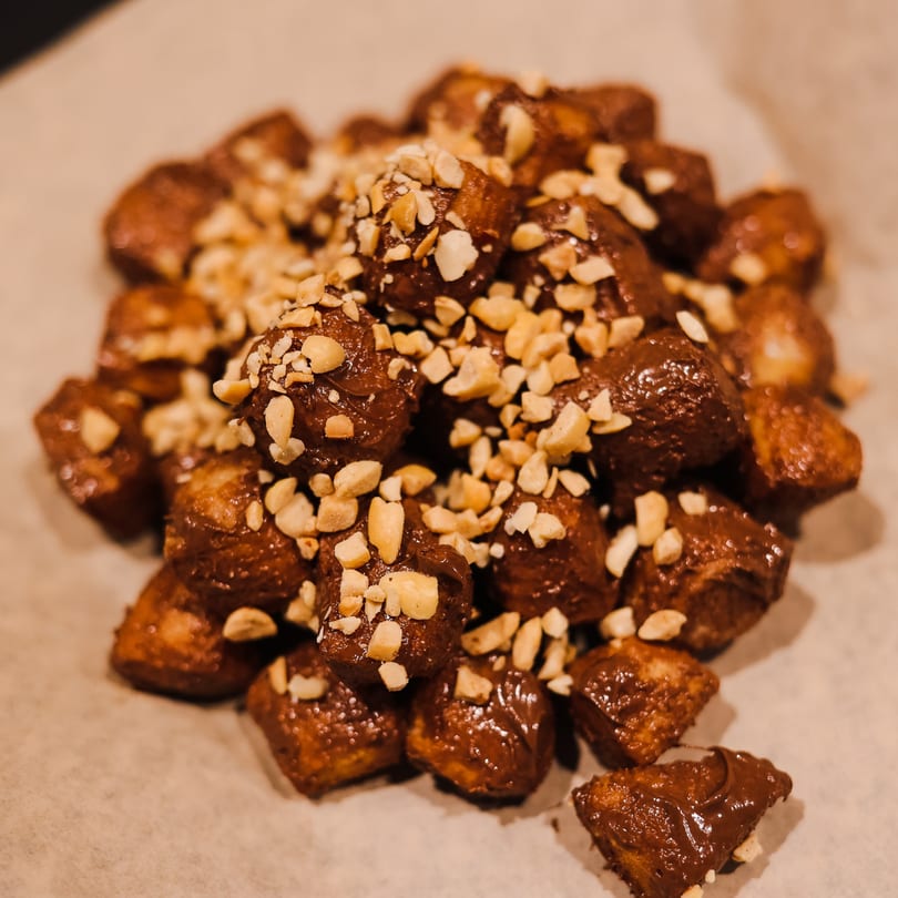 Close-up of Greek Loukoumades, golden-brown dough balls drizzled with chocolate and sprinkled with nuts.