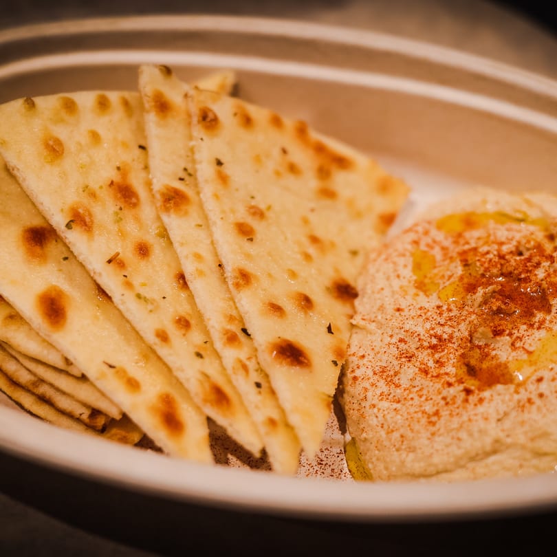 Warm pita bread triangles and creamy hummus drizzled with olive oil and paprika in a bowl.